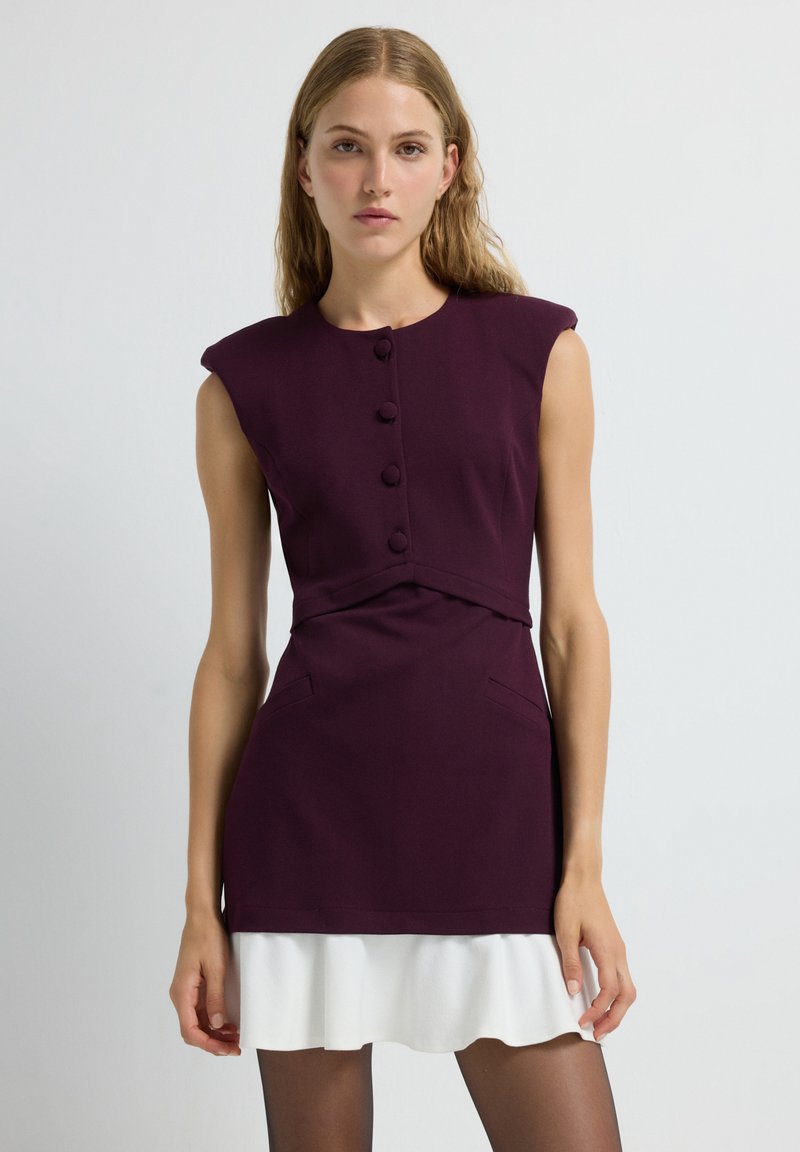 Robe courte d'un bordeaux profond avec des manches courtes, des détails de boutons et un ourlet en volants blancs superposés. Tissu lisse avec poches latérales.