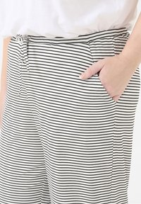 Shorts en tissu doux à rayures noires et blanches, dotés d'une taille élastique, d'un cordon de serrage et de poches latérales. Les rayures horizontales ont une largeur uniforme.