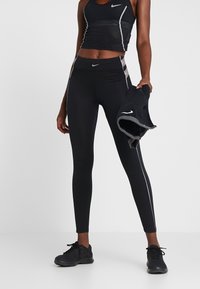 Czarny sportowy crop top i legginsy z odblaskowymi akcentami. Legginsy są dopasowane i smukłe, w zestawie z ciemnym ręcznikiem.