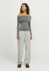 Siva off-the-shoulder bluzica s dugim rukavima i nabranim detaljima, u kombinaciji sa svijetlopljim baggy trapericama i smeškim cipelama bez pertli.