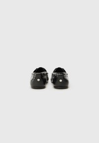 Schwarze Lederballerinas mit glatter Textur, Rückansicht zeigt silberne Hardware-Akzente und ein kreisförmiges Logo-Detail auf der Rückseite.