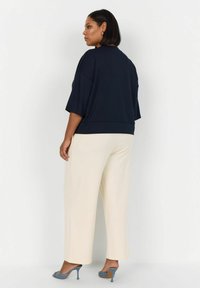 Námornícky oversized top s krátkymi rukávmi, spojený s smotanovými širokými nohavicami. Modelka má na sebe šedé vysoké topánky. Hladká textúra látky.
