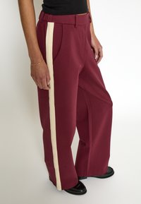 Burgundy wide-leg pants with a cream vertical stripe, featuring a relaxed fit, elastic waistband, and side pockets.