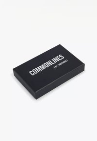 Sort rektangulær boks med hvid tekst "COMMONLINES [ BY / BROTHERS ]" øverst, placeret på en hvid overflade.