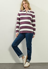 Langarm-Polohemd in lila und weißen Streifen mit Kragen, kombiniert mit dunkelblauen Jeans und weißen Sneakers mit beige Farbakzenten.