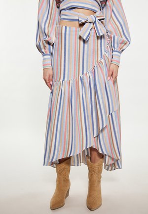 Vrouw draagt een multicolor rok met verticale strepen en een bijpassend topje met strik, gecombineerd met beige suède cowboylaarzen tot halverwege de kuit.