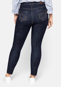 Vaqueros ajustados azul oscuro de mezclilla con una textura suave, que cuentan con dos bolsillos traseros con costura curvada y una cintura alta.