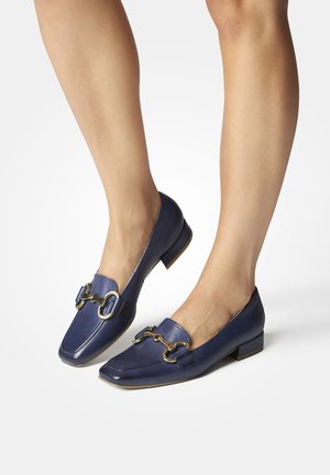 Navy blue leather loafers with a flat heel, featuring gold-tone hardware and a decorative buckle design on the front. Smooth finish.