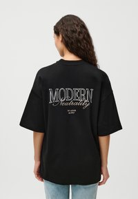 Sort oversized T-shirt med broderet tekst på ryggen: "MODERN Neutrality BY LEGGER est. 2017." Blød stof og afslappet pasform.