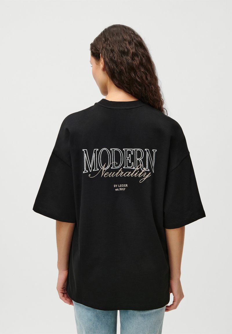 Sort oversized T-shirt med broderet tekst på ryggen: "MODERN Neutrality BY LEGGER est. 2017." Blød stof og afslappet pasform.