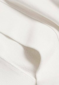Biely textil s hladkou štruktúrou, s jemnými ryhami a prehnutými miestami, ktoré zdôrazňujú jemné splývanie a detaily stehov.