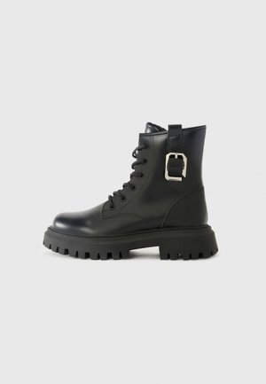 Schwarze Lederknöchelstiefel mit einer klobigen Sohle, Schnürverschluss an der Vorderseite und einem seitlichen Schnallenakzent. Glatte Textur und schlankes Design.