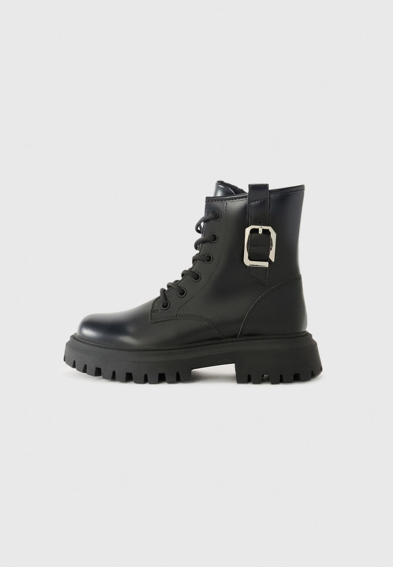 Botas de tobillo de cuero negro con suela gruesa, cordones en la parte delantera y un detalle de hebilla lateral. Textura suave y diseño aerodinámico.