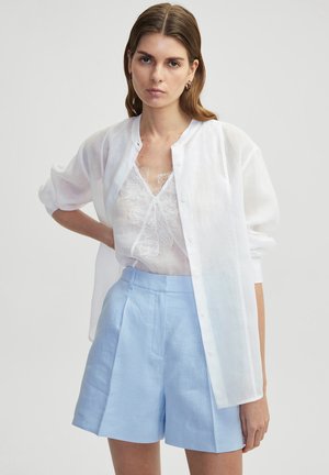 Witte lichte button-up blouse over een doorschijnende witte kant camisole, gecombineerd met lichtblauwe high-waisted shorts. Glad textuur, ontspannen pasvorm.
