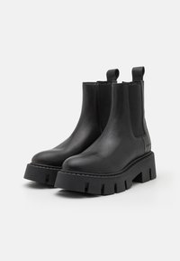 Sorte svarte lærankle støvler med kraftige plattformsåler, med elastiske sidepaneler og trekkalternativer for enkel påkledning. Teksturert overflate med sømdetaljer.
