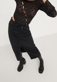 Haut en dentelle noire avec des détails découpés, associé à une jupe midi en jean noire avec une fente latérale, porté avec des bottes noires hautes à talons.