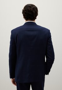 Giacca da abito a quadri blu navy vista da dietro, con una vestibilità strutturata, revers a punta e una leggera lucentezza nel tessuto.