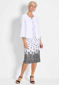 Weißes, tailliertes Sakko über einem gemusterten schwarz-weißen Kleid mit floralen Motiven. Das Kleid hat einen knielangen Saum und eine subtile Textur. Schwarze Sandalen.