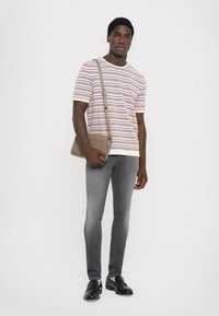 Ριγέ, κοντομάνικο T-shirt σε λευκό, μπλε και πορτοκαλί. Στενά γκρι τζιν. Κρατώντας μια μπεζ τσάντα χιαστί. Μαύρα loafers. Θέση σε στάση.