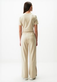 Beżowy, dwuczęściowy zestaw składający się z koszulki z krótkim rękawem oraz szerokich spodni z elastycznym pasem i bocznymi rozcięciami, wykonany z gładkiego materiału.