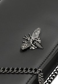 Borsa a tracolla in pelle nera con un'inserto a forma di ape in argento e una tracolla in catena argentata, caratterizzata da dettagli in superficie testurizzati.