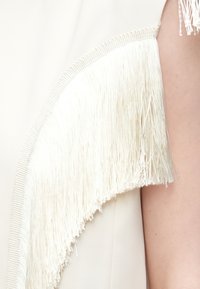 Valge riideese, millel on käiseõmblusel tekstureeritud kreemjas tutike. Kangas on sile ja õrna läikega.