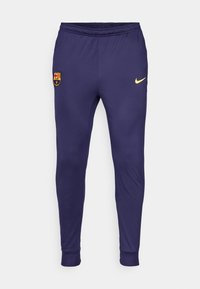 Marineblauwe sportbroek van soepel stof met een aansluitend ontwerp. Voorzien van een gele Nike-logo en een Barca-embleem op de linkerbeen.