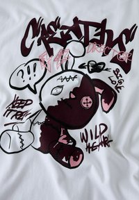 Bawełniany t-shirt z grafiką w kolorze białym, przedstawiający kreskówkowego króliczka w burgundowym i różowym kolorze z napisami. Do wyróżniających się detali należą guziki i szwy.