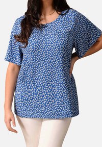 Modrý top s květinovým vzorem a krátkými rukávy, kulatým výstřihem a vyrobený z lehkého materiálu. Má malé bílé květiny. Nosí se s bílými kalhotami.