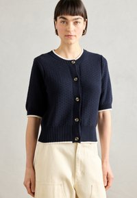 Navy blue short-sleeve cardigan with textured knit design, ribbed hem, and contrasting cream trim. Features five round buttons.