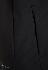 Schwarze, wasserfeste Jacke mit glatter Textur, ausgestattet mit einer Reißverschlusstasche und dezentem Markenlogo, entworfen für Outdoor-Aktivitäten.
