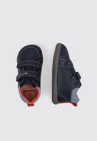 Zapatos infantiles de color azul marino con correas de Velcro, detalles grises y forro interior naranja. Punta redondeada y suela flexible gris con orificios de ventilación.