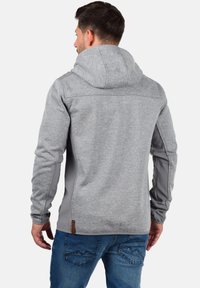 Haut à capuche pour hommes en tissu gris avec une capuche, présentant des panneaux latéraux gris clair et un accent logo près de l'ourlet, texturé pour le confort.