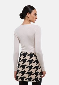 Un haut à manches longues beige clair associé à une mini-jupe en motif pied-de-poule noir et beige, présentant une coupe ajustée et une texture lisse.