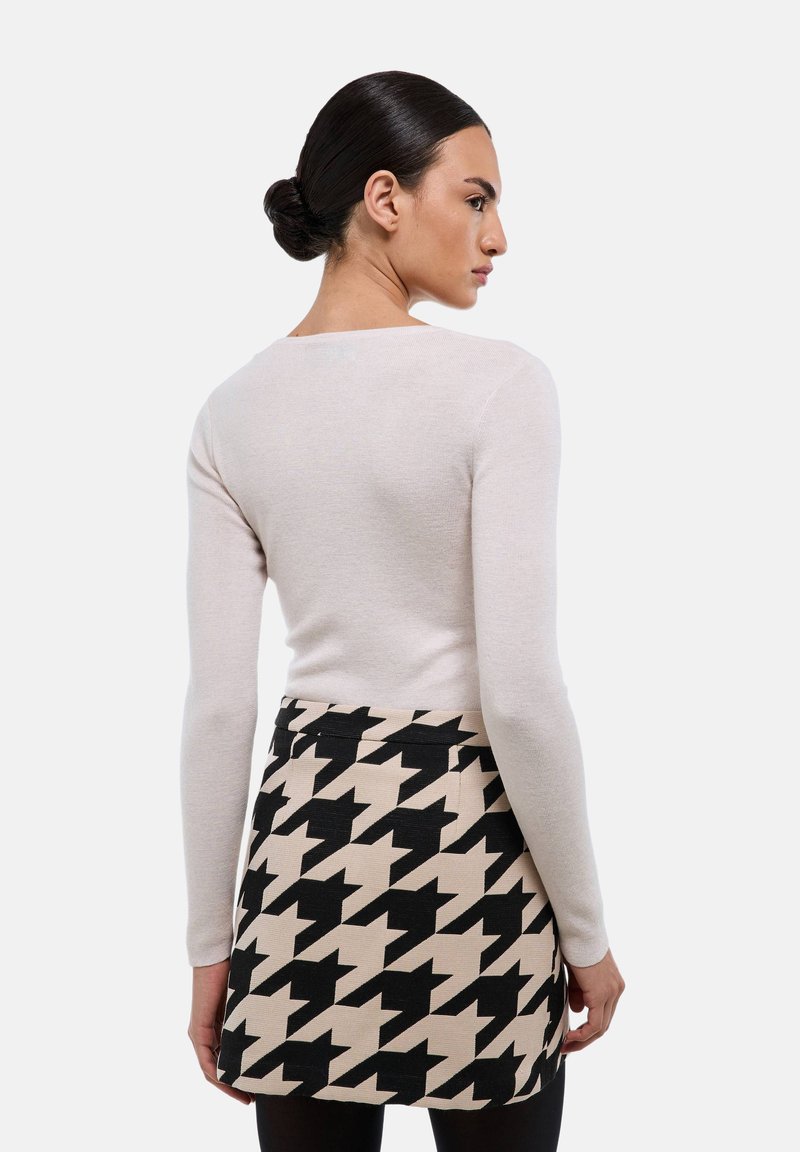 Un haut à manches longues beige clair associé à une mini-jupe en motif pied-de-poule noir et beige, présentant une coupe ajustée et une texture lisse.