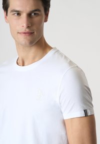 T-shirt bianco a maniche corte realizzato in cotone. Presenta un logo in rilievo discreto sul petto e un accento nero a contrasto sulla manica.