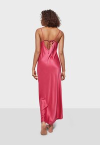Long, pink satin nightgown with adjustable spaghetti straps, featuring a low-cut back secured by a tie detail. Smooth, glossy texture.