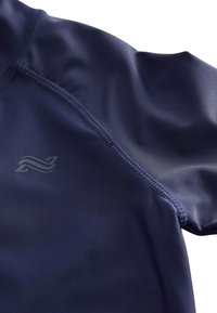 Sügavsinine sportlik tipp, mis on valmistatud siledast ja venivast kangast, millel on õmblusteta ühendused ning vasakul rinnal peen logo.