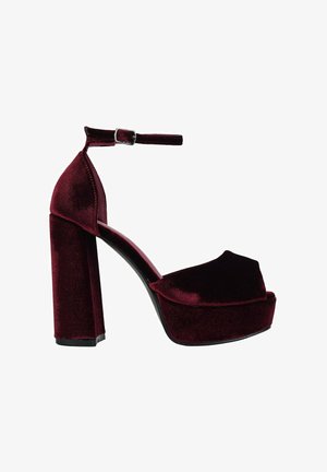 Sandalia de tacón alto de terciopelo burdeos con una plataforma gruesa, correa en el tobillo y tacón cuadrado. Textura suave con un mínimo de detalles en metal.
