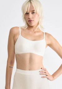 Vaaleanbeige bralette, jossa on ohuet hihnat, saumatonta muotoilua, pehmeä pinta ja pyöreä malli, yhdistettynä matching korkeavyötäröiseen alaosaan.