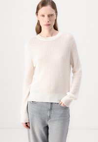 Lett, ribbet strikket genser i myk hvit, med rund hals og lange ermer. Brukt sammen med grå, avslappet passform jeans.