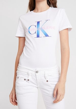Bílý bavlněný tričko s velkým modrým a růžovým logem "CK" a textem "CALVIN KLEIN JEANS" pod ním, kulatým výstřihem a krátkými rukávy.