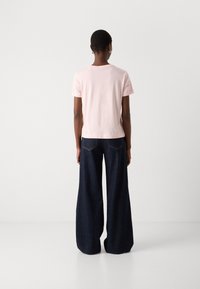 T-shirt en coton rose clair à manches courtes, associé à un pantalon en denim large bleu foncé. Présente un design simple et épuré.