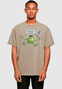 Beige übergroßes T-Shirt aus Baumwolle, mit einem Grafikdesign eines grünen Charakters aus Monsters University und Textdetails.