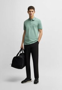 Mint green polo shirt with collar and three buttons, worn with black trousers. Black sports shoes and a black duffel bag are included.