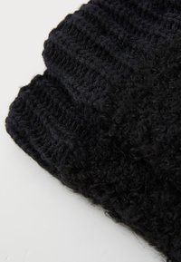 Bonnet en tricot noir fait de fil doux. Présente une texture côtelée et un design volumineux avec une apparence légèrement duveteuse.