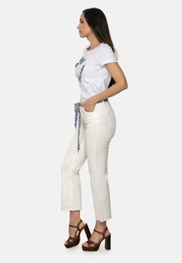 Camiseta blanca con gráfico azul, pantalones blancos de cintura alta con un cinturón atado y tacones de plataforma marrones. Tejido suave y corte ajustado.