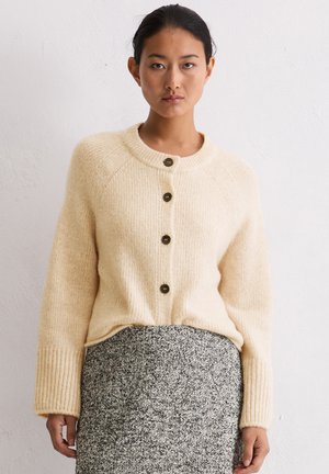 Gebreide crèmekleurige cardigan met een ronde hals, een sluiting met vijf knopen aan de voorkant, geribde manchetten en een gestructureerde stof. Gedragen over een gestreepte grijze rok.