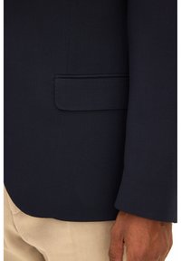 Marinblå blazer med texturerat tyg, enkel bröstficka och skräddarsydd passform, visas intill ljusbeige byxor och en hand.