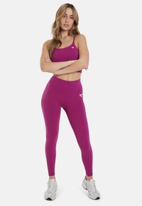 Magenta sportski grudnjak i visoko rezane tajice napravljene od rastezljivog materijala, sa malim bijelim logotipom na lijevoj strani grudnog koša i na bedro.